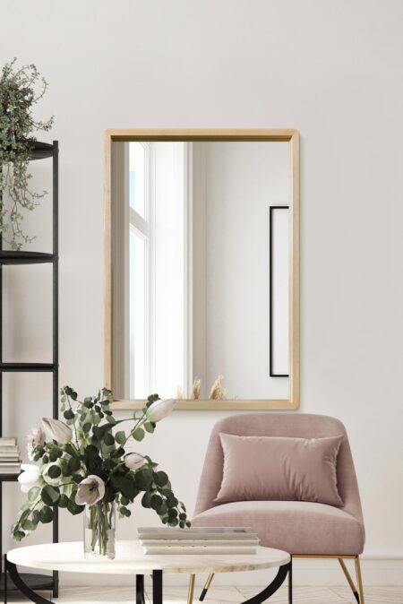 Oak framed rectangular mirror hung above a pink velvet armchair in a bright living room