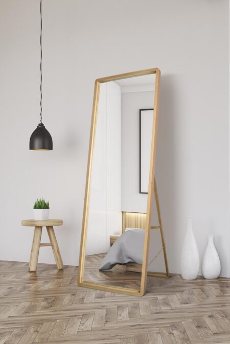 Oak framed full length mirror leaning against a white wall in a bright Scandinavian-style bedroom