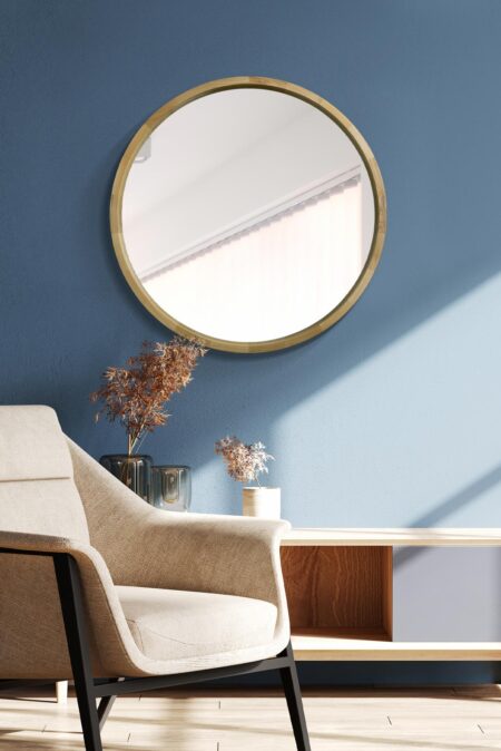 Round wooden framed mirror with natural oak finish mounted on a blue wall above a linen armchair