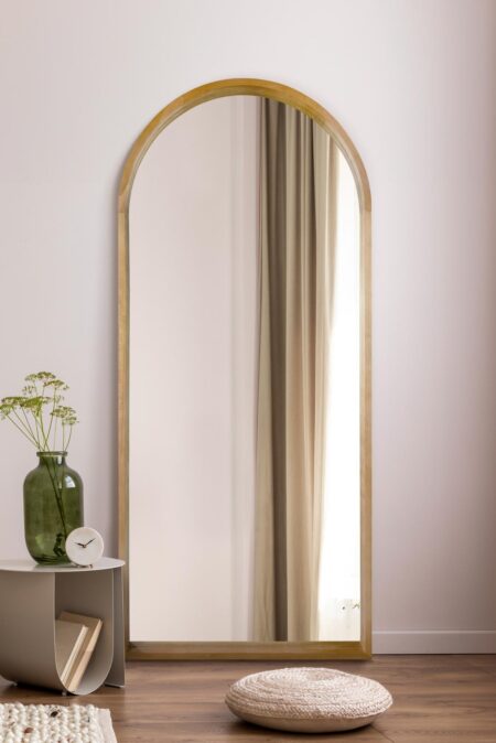 Oak framed full length wall mirror leaning against a pale wall in a styled room