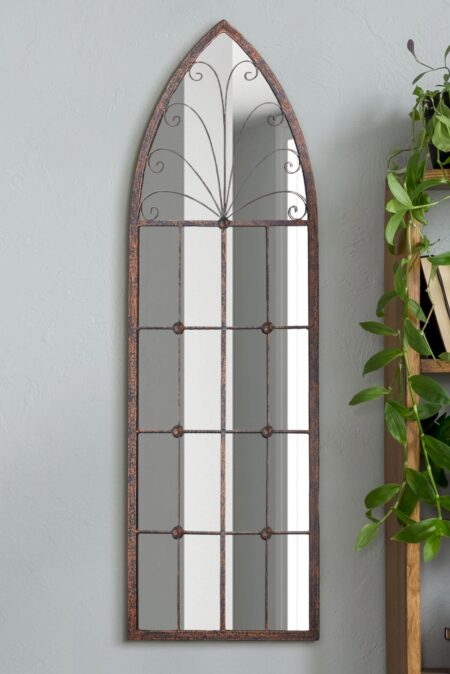 Gothic arch mirror with distressed copper-finish frame leaning against an interior wall