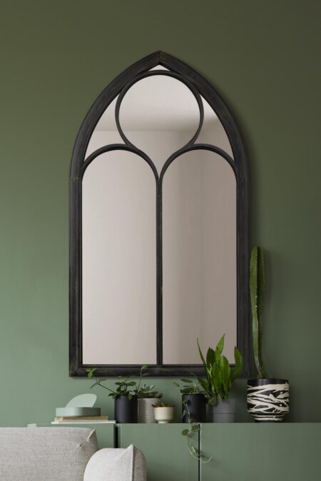 Tall Gothic arch mirror with distressed black frame styled above a green console table indoors