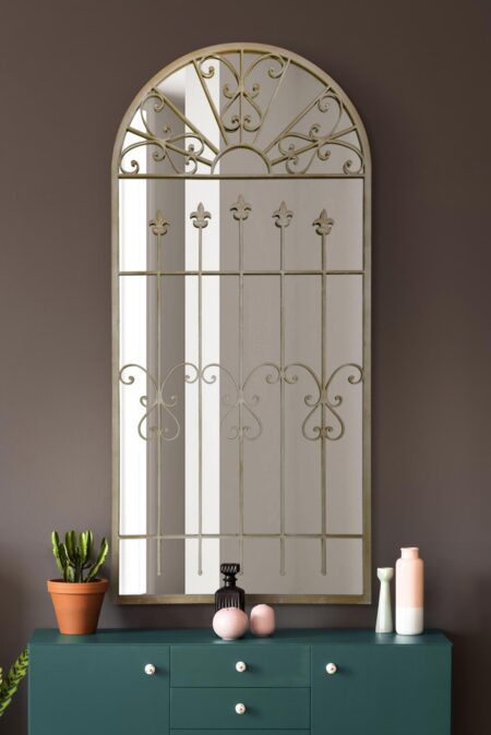 Large arched ivory mirror with fleur-de-lys and scroll metalwork above a teal sideboard