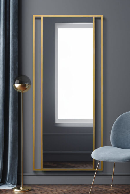 Tall gold twin-bar mirror leaning against a dark grey wall in a contemporary styled room