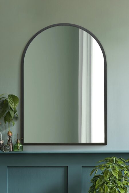 Large arched black-framed mirror displayed above a teal painted fireplace mantel