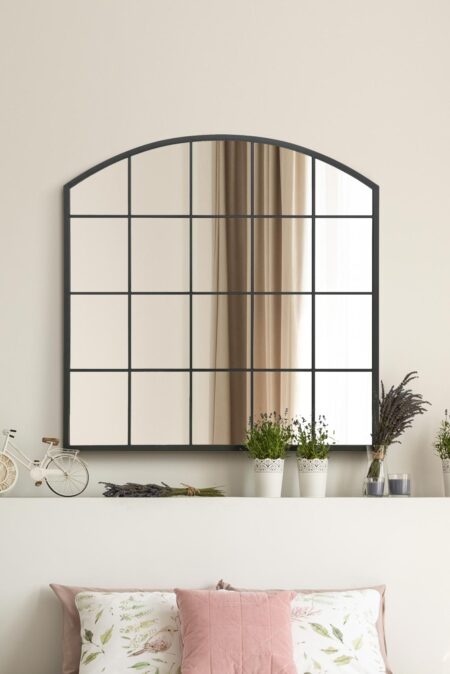 Arched window-style mirror with black grid frame styled above a living room shelf with lavender