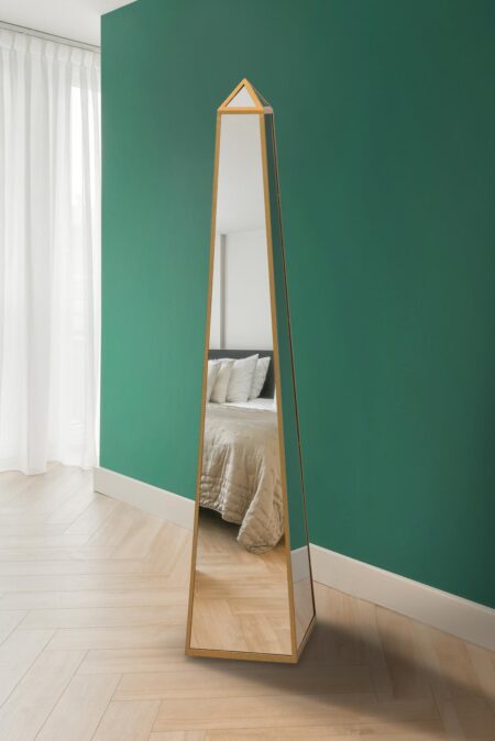 Gold free standing mirror with obelisk pyramid shape against a teal bedroom wall