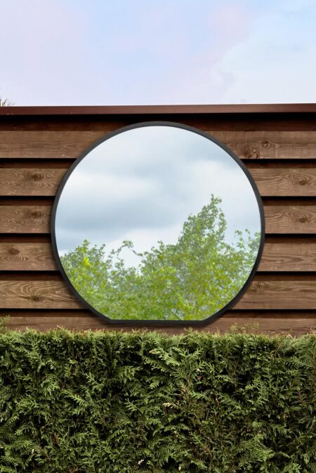 Large black round wall mirror with flat bottom mounted on a timber garden fence