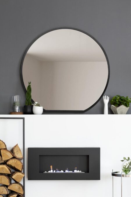 Round black-framed mirror styled above a modern fireplace on a grey living room wall