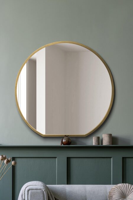 Round mirror with a slim brushed gold frame displayed above a sage green console in a living room