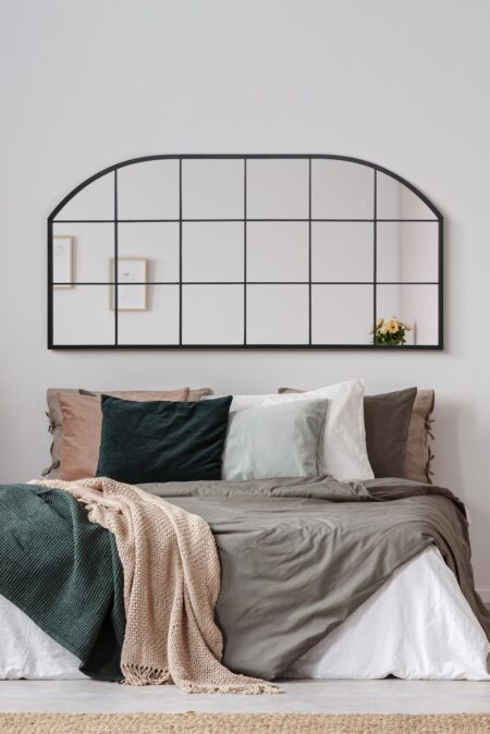 Wide arched black grid mirror displayed above a layered neutral-toned bed in a calm bedroom