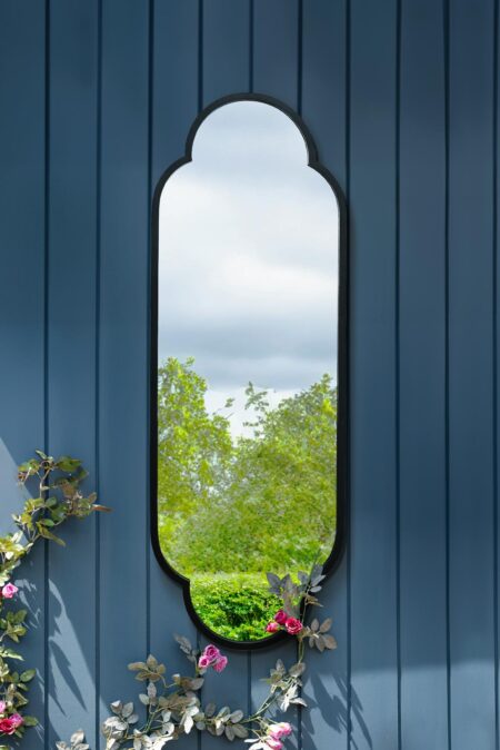 Black steel scalloped mirror full length mounted on a blue garden wall with climbing roses