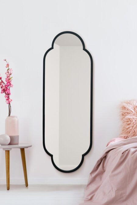 Tall black scalloped wall mirror styled in a soft pink bedroom next to a bedside table