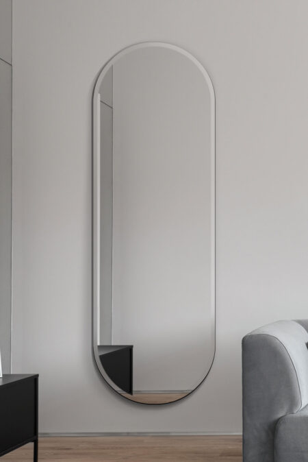 Pill shaped mirror full length frameless design hung vertically on a grey living room wall