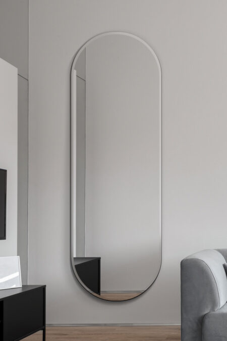 Retro frameless mirror with capsule shape hung full length on a grey living room wall
