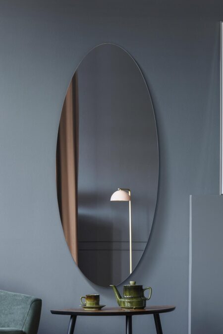 Large oval wall mirror styled above a wooden side table with green ceramics and a pink lamp