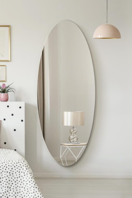 Large oval full length mirror hung on a white bedroom wall above a polished floor