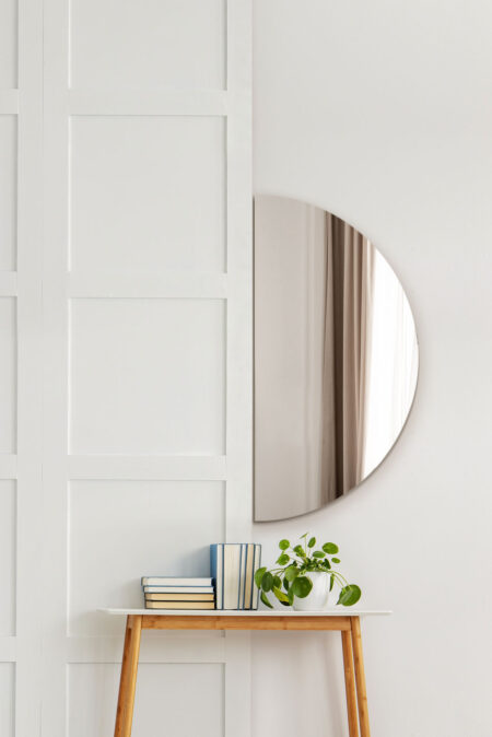Frameless semicircle mirror hung above a white console table with books and a plant
