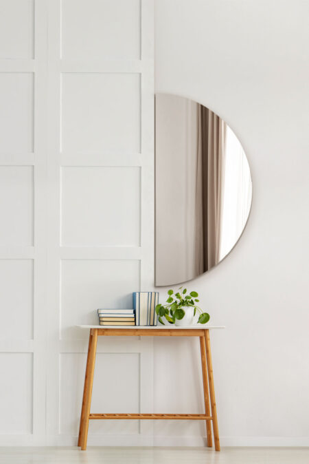 Large frameless half circle wall mirror hung above a wooden console table