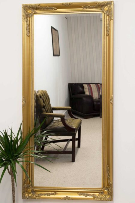 Extra large gold leaner mirror displayed upright against a white living room wall