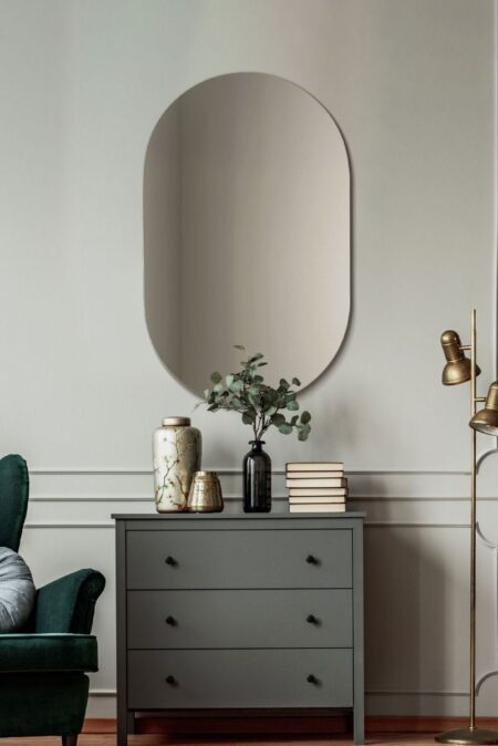 Frameless oval wall mirror hung above a grey chest of drawers in a elegant living room