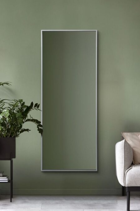 Tall silver leaner mirror with slim brushed aluminium frame hung on a sage green wall